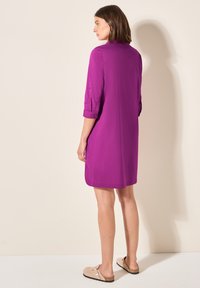 Abito viola al ginocchio con maniche a tre quarti, polsini con bottoni e una vestibilità rilassata. Abbinato a scarpe beige slip-on.