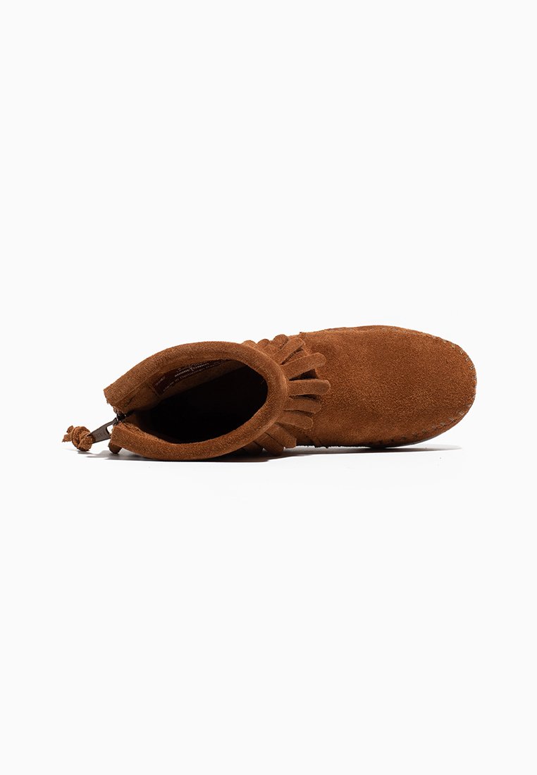 Mocasín de ante marrón hasta el tobillo con detalle de flecos alrededor de la abertura, interior visible y suela cosida sobre un fondo blanco.