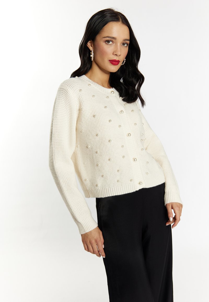 Witte gebreide cardigan met gestructureerde stof, ronde hals en parelaccenten, gecombineerd met zwarte satijnen broeken.
