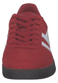Sneaker en suède rouge avec des rayures diagonales blanches, présentant des lacets ronds, une languette texturée et une semelle en caoutchouc noir.