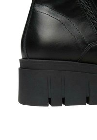 Stivale alla caviglia in pelle nera con suola spessa nera, caratterizzato da dettagli intagliati e cuciture diagonali. Dettaglio con zip sul lato.