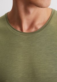 Olivenfarbendes T-Shirt aus weichem Stoff mit Rundhalsausschnitt und subtilen Texturmuster, das über eine glatte Oberfläche und keine sichtbaren Logos oder Akzente verfügt.