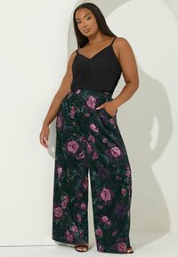 Blommiga vida byxor i mörkgrön med mönster av lila och rosa blommor. Kombineras med en svart linne. Har sidofickor och elastisk midja.