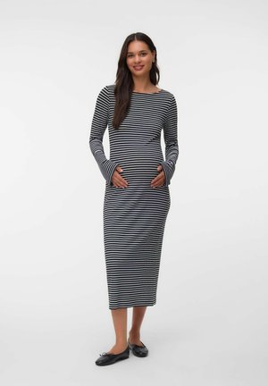 Woman smiling wearing a black and white horizontal striped long-sleeve midi dress and black ballet flats, standing with hands on her belly.