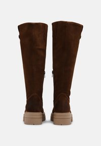 Bruine suède kniehoge laarzen met een ronde neus, ton-sur-ton stiksels en een lage rubberen zool. Bevat een knoopdetail en zijritsen.