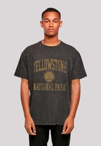 Black cotton oversized t-shirt featuring a yellow graphic text "YELLOWSTONE NATIONAL PARK" and a circular logo in the center. Crew neckline.