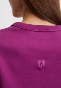  Paarse katoenen t-shirt met een ronde hals, een gladde textuur en een subtiele geborduurde logo op de achterkant. Vlakke stikseldetails zichtbaar.