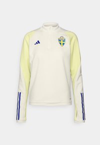 Pullover bianco a maniche lunghe con dettagli gialli, presenta un colletto con zip a metà, strisce blu sulle maniche e un emblema svedese sul petto.