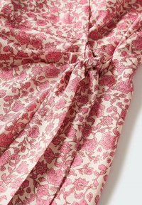 Blouse fleurie en tissu doux, avec une base rose pâle ornée de motifs floraux rose foncé, détail froncé et accent noué à la taille.