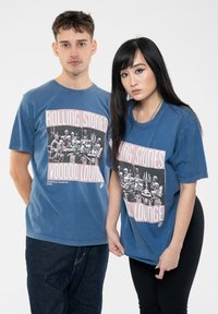 Blue cotton t-shirts featuring a graphic print of skeletons and the text "Rolling Stones Voodoo Lounge," with short sleeves and a relaxed fit.
