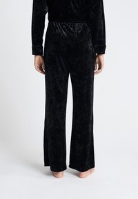 Pantalones de terciopelo negro de pierna ancha con una textura suave, cinturilla elástica y un acabado pulido. Presenta un ajuste relajado y una silueta acampanada.