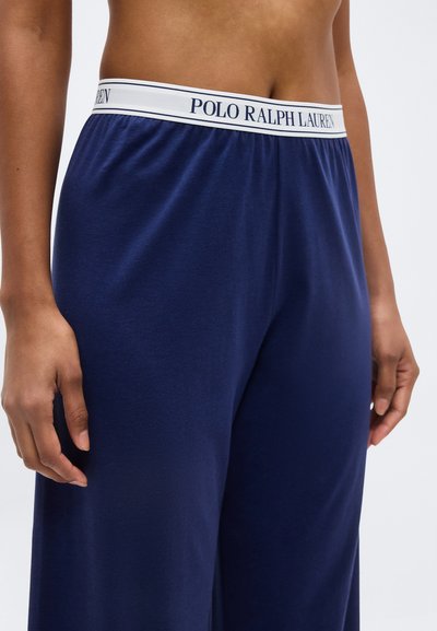 Κοντινό πλάνο ενός ατόμου που φοράει μπλε σκούρο παντελόνι με λευκή ελαστική ζώνη μέσης που αναγράφει το κείμενο "Polo Ralph Lauren".