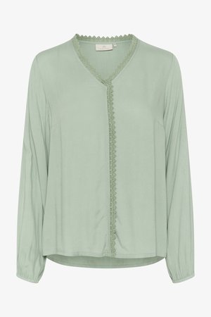 Šviesiai žalia palaidinė su ilgomis rankovėmis, V formos iškirpte ir dekoratyvine nėrinių apdaila per centrą. Audinys turi lygų, švelnų tekstūrą.