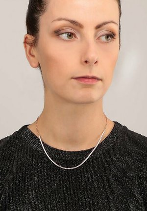 Dünne Silberkette, die über einem schwarzen, strukturierten Pullover getragen wird. Die Kette verfügt über kleine, funkelnde Akzente, die in einem zarten Muster angeordnet sind.