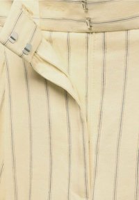 Light yellow striped pants with blue and orange lines, featuring a zip fly and metallic hook closure. Soft, textured fabric.