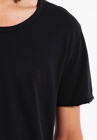 Zwarte t-shirt met korte mouwen van katoen, met een ronde hals en onnabouwde mouwranden. Zachte textuur met een eenvoudig ontwerp.