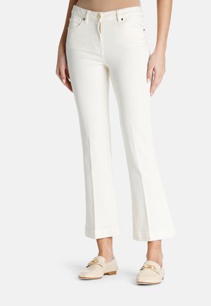 Weiße Schlagjeans mit Fronttaschen, einem Knopf- und Reißverschluss und einer glatten Textur. Kombiniert mit beigen Loafers mit goldenen Beschlägen.