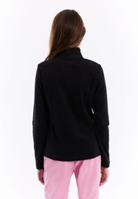 Zwarte fleecedeken met hoge kraag, lange mouwen en een getailleerde pasvorm, gedragen met lichtroze broek. Glad textuur, geen zichtbare patronen.