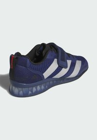 Blå træningssko med tekstureret mesh-overdel, hvide striber, justerbar rem og gennemsigtig mønstret sål. Bagsiden har rød branding.