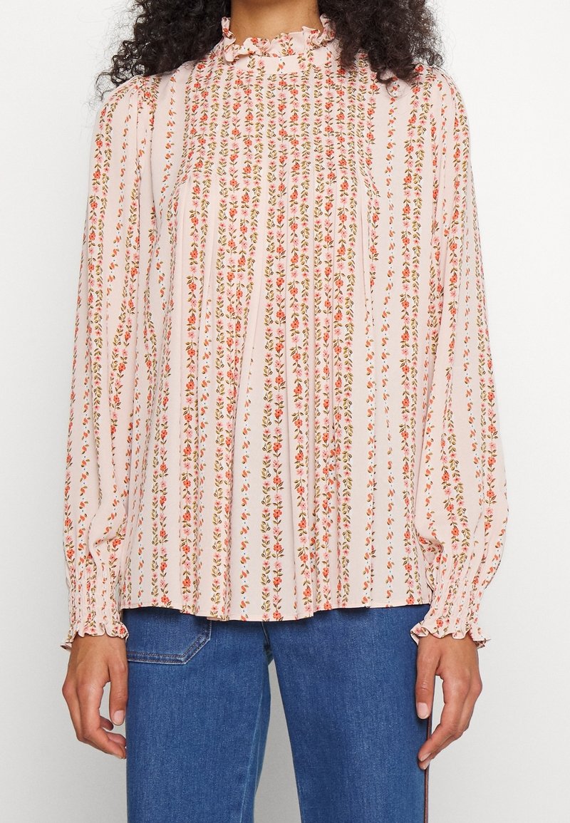 Blouse à manches longues et col montant avec des rayures verticales fleuries rose et rouge, associée à un jean en denim bleu.