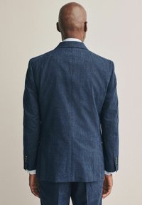 Sacou din stofă cu model bleu marin, cu o croială ajustată, material texturat și două butoane pe manșete; văzut din spate.