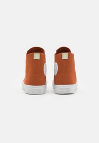 Ténis de cano alto em lona laranja com solas de borracha branca e detalhe de marca na parte traseira e nas laterais. Textura suave, design sem costuras.