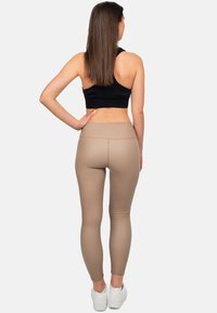 Top corto nero e leggings a vita alta beige, caratterizzati da una texture liscia e un design aderente, indossati con sneaker bianche.
