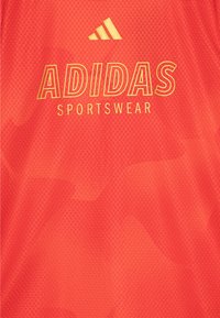Rød Adidas sportsklærstoff med et teksturert mønster, med stor gul "ADIDAS" logo og mindre merke over.