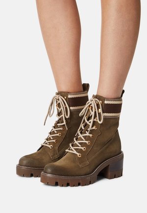 Bottines en daim marron à talon chunky, avec œillets dorés, lacets beiges et un revers en tricot avec des accents rayés.