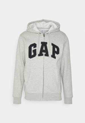Šedá mikina s kapsou na klokanku a zipem, s černým logem "GAP". Měkká látka a nastavitelné stahovací kapuce.