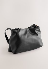 Mustast nahast käekott pehme ja lõdva disainiga. Varustatud kahe sangaga ja tagasihoidlike metalldetailidega. Sile tekstuur ja minimaalne õmblemine.