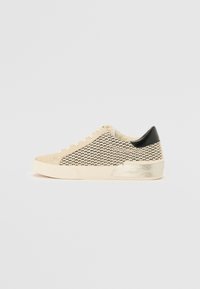 Sneaker beige e nera con motivo, punta strutturata, lacci crema e un accento nero sul tallone. Presenta un dettaglio in argento metallico sulla suola.