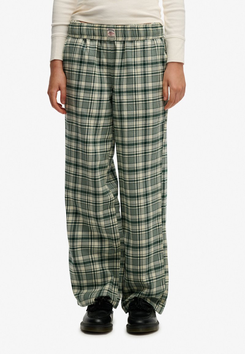 Pantalones de pijama a cuadros verdes y crema con un ajuste relajado, cinturilla elástica y textura de tela suave. Combinados con zapatos negros.