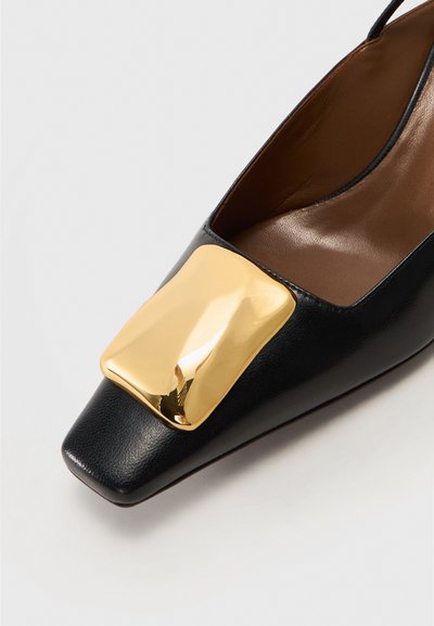 Black leather shoe with a square toe and a large gold metallic accent on the vamp. Smooth texture with a modern design.