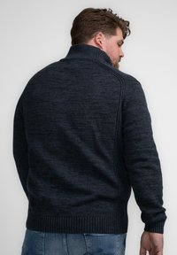 Donkerblauwe gebreide trui met een hoge kraag, voorzien van een textuurpatroon en ribbels aan de onderkant. Een relaxte pasvorm met lange mouwen.