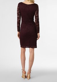 Burgundy spetsklänning med långa ärmar, figurnära design och knälång fåll. Har en dragkedja bak och scallopade kanter. Bärs med nakna högklackade skor.