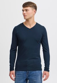 Langärmliges navy V-Ausschnitt-Shirt aus weichem Stoff, mit einer figurbetonten Silhouette und glatter Textur, kombiniert mit blauen Denim-Jeans.