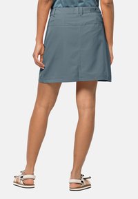 Světle modrá, lehká sukně s vypasovaným pasem a jemnými detaily prošití, doplněná o bílé sandály s černými akcenty.