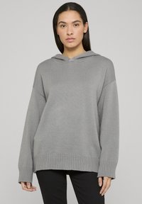 Sweat à capuche tricoté gris avec une coupe ample, ourlet côtelé et manches retroussées ; présente un design simple, sans ornements et une texture douce.