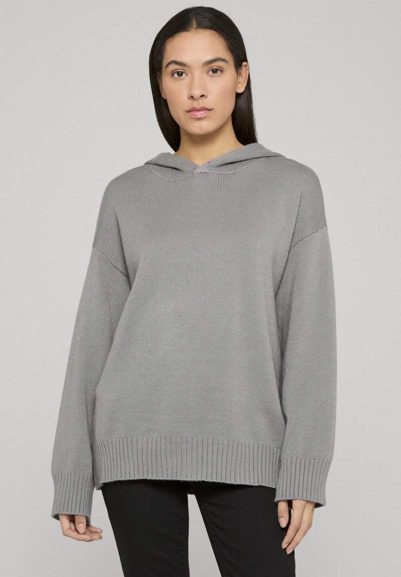 Sweat à capuche tricoté gris avec une coupe ample, ourlet côtelé et manches retroussées ; présente un design simple, sans ornements et une texture douce.