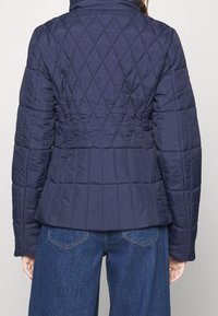 Granatowa pikowana kurtka puchowa, z wysokim kołnierzem, wzorem w romby oraz dopasowaną talią z falbanką. Miękka, gładka faktura.