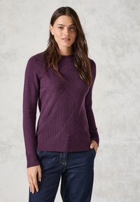 Violetti neulepusero, jossa on teksturoitu timanttikuvio, pitkät hihat, pyöreä kaula-aukko ja resorireunus. Yhdistetty tummansinisiin farkkuihin.