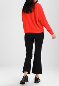 Sudadera roja de gran tamaño con hombros caídos, combinada con pantalones negros acampanados. Zapatillas negras completan el conjunto. Diseño sencillo y casual.