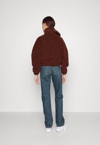 Brun kunstpelsgenser med høy krage, løs passform og ribbete nederkant, kombinert med høyt liv blå jeans og hvite sneakers.