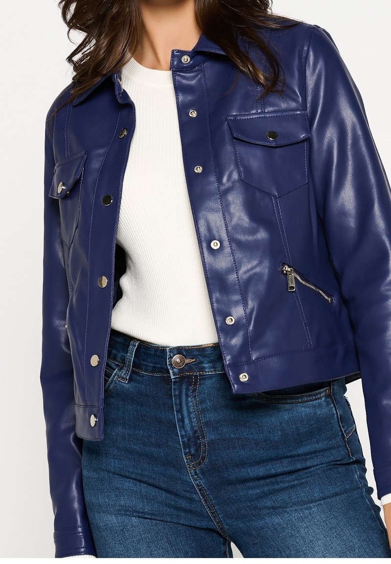 Giacca cropped in pelle blu navy con bottoni a pressione e due tasche sul petto. Presenta una tasca laterale con zip e una texture liscia e lucida.