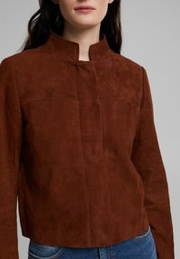 Bruine suède cropped jas met staande kraag, voorzien van een gladde textuur, subtiele stikdetails en een minimalistisch ontwerp.