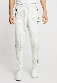 Vita joggers med ett blommönster, avsmalnande design, elastisk midja, dragsko, sidofickor och svarta Nike-logoförstärkningar.