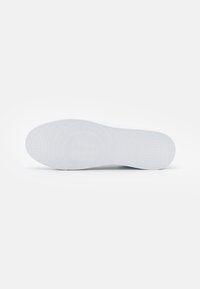 Weißer Gummischuhsohle mit texturierten kreisförmigen Mustern und Rillen für besseren Halt. Glatte Oberfläche mit abgerundetem Zehenbereich und flachem Absatzdesign.