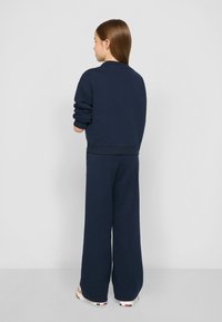 Sudadera azul marino y pantalones de pierna ancha de tela suave, con puños y cinturilla acanalados, vistos desde la parte de atrás.