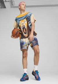 Trykt oversized t-shirt med et løvegrafik, parret med farverige shorts med svulmuster. Iført blå og gule træningssko.